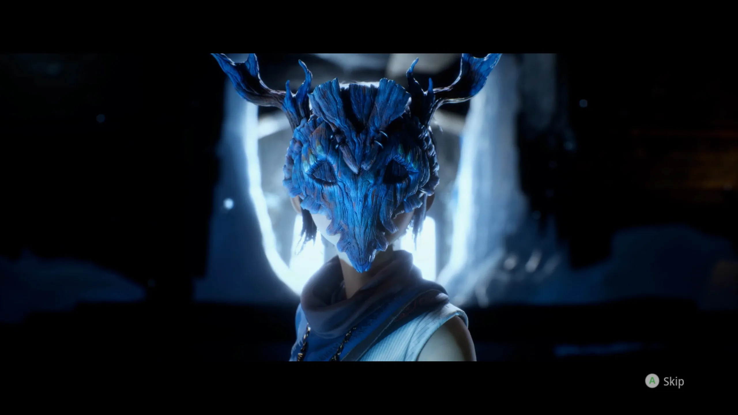 A cinematic cutscene from Kena: Bridge of Spirits showing a close-up of a character wearing an elaborate blue wooden spirit mask with antler-like horns and intricate carved textures. The figure is backlit by a bright ethereal glow, creating a dramatic, mysterious atmosphere. A “Skip” prompt is visible in the bottom-right corner.