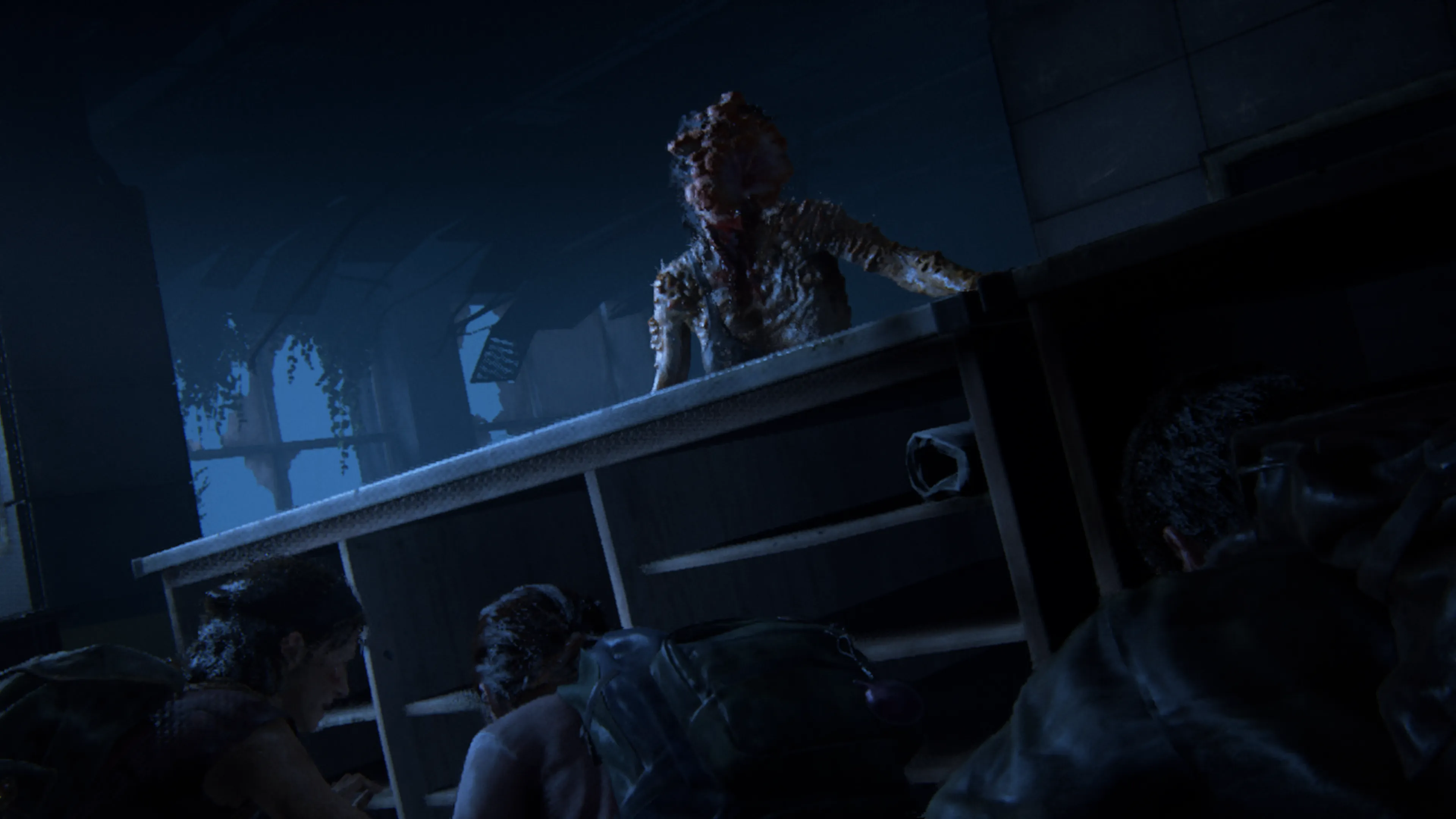 A dark, tense scene showing fungal-infected creatures known as clickers in a dimly lit abandoned building, with one standing atop office furniture while others lurk below, their heads grotesquely disfigured by fungal growth that has replaced their faces