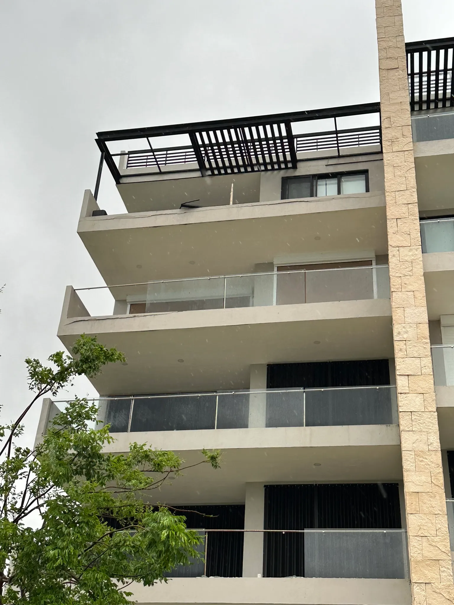 Damage to the condo building showing several glass panes completely gone, others cracked, and cracks in the concrete