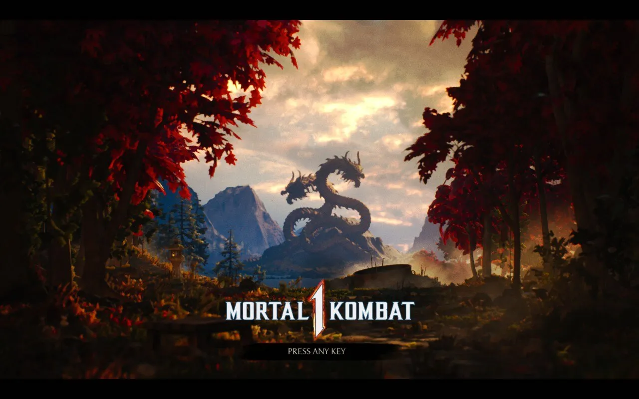 A scenic landscape featuring a pathway flanked by trees with red leaves, leading towards a distant mountain range. In the center, a large, two-headed dragon statue dominates the horizon. The foreground displays the title MORTAL KOMBAT 1 in bold white letters with a subtle metallic sheen. Below the title, the text PRESS ANY KEY prompts the viewer to interact.