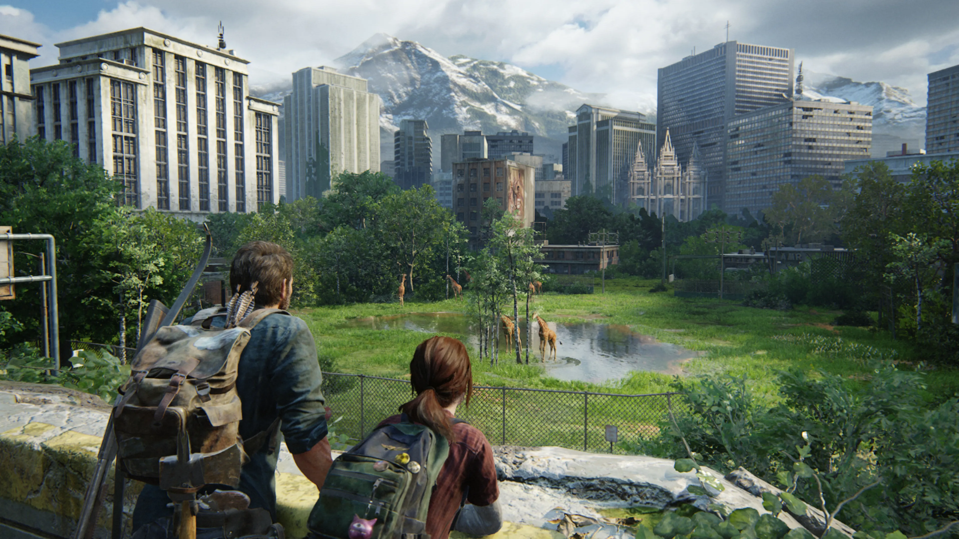 Two characters with backpacks stand on an overgrown rooftop viewing a post-apocalyptic cityscape where nature has reclaimed urban spaces, with giraffes grazing near a small pond in what was once a city park, modern buildings and a classical temple visible against snow-capped mountains in the background